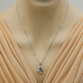 Silver necklace with a pendant on a mannequin wearing a beige dress.